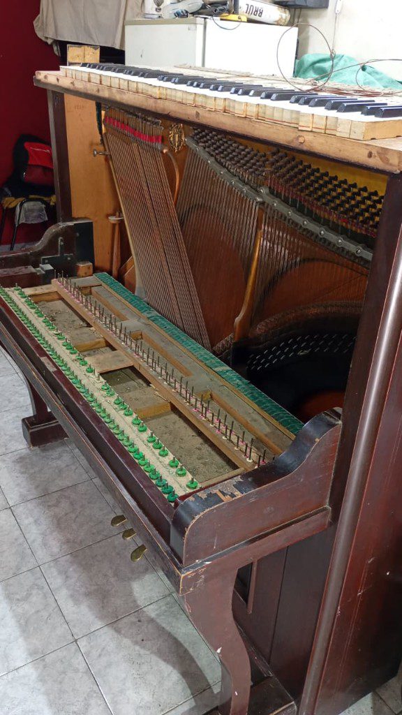 Clavijas y cuerdas de un piano vertical durante la afinación, con el teclado levantado